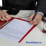 Бизнесмен подписывает документы в красной папке