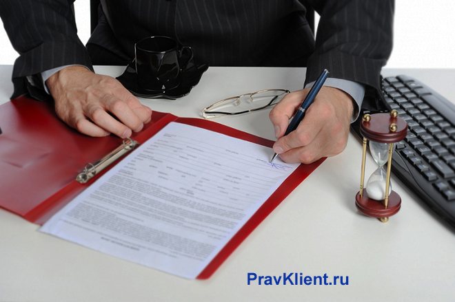 Бизнесмен подписывает документы в красной папке